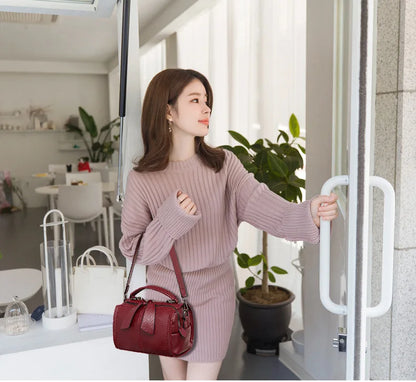 Woman in a pink outfit holding a red handbag in an indoor setting.